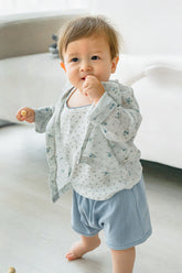Toddler in Avauma Littleshell forest mint cardigan and light blue bloomers, holding a wooden spoon.